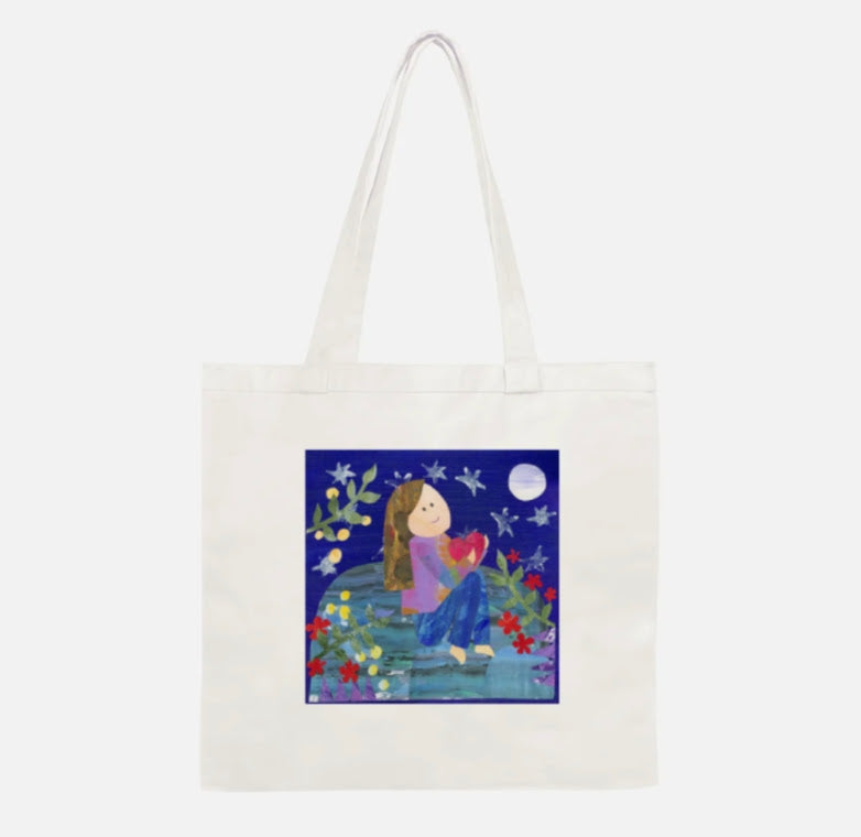 A cream canvas tote bag with a square colorful illustration printed on the front, featuring a girl sitting on a bench under a full moon surrounded by flowers.