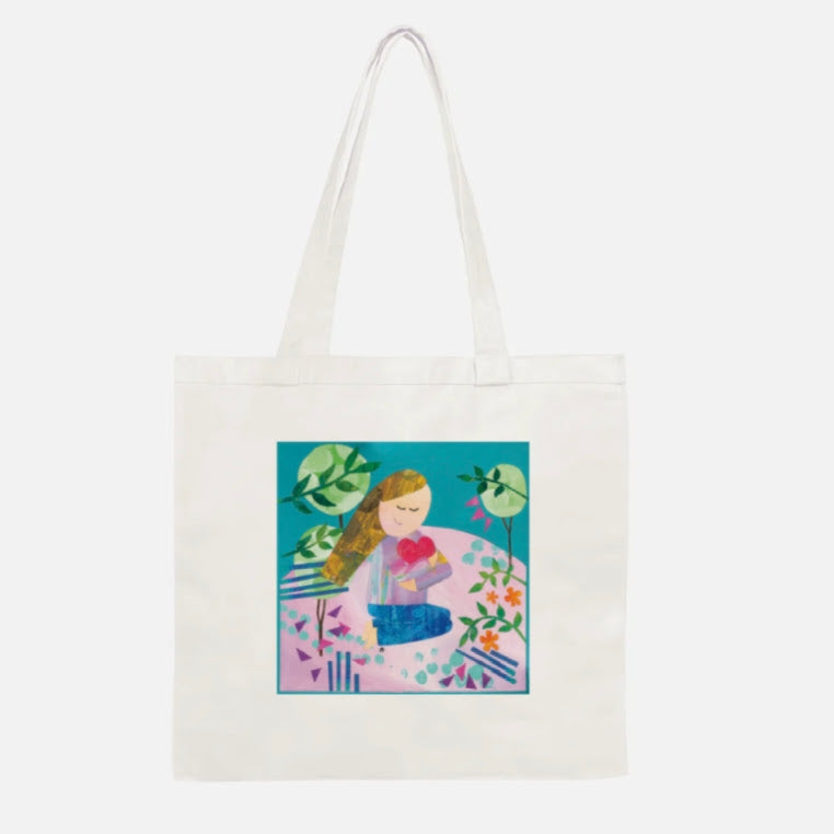 An off-white canvas tote bag with long handles, featuring a colorful square graphic print on the front of a girl meditating surrounded by plants.